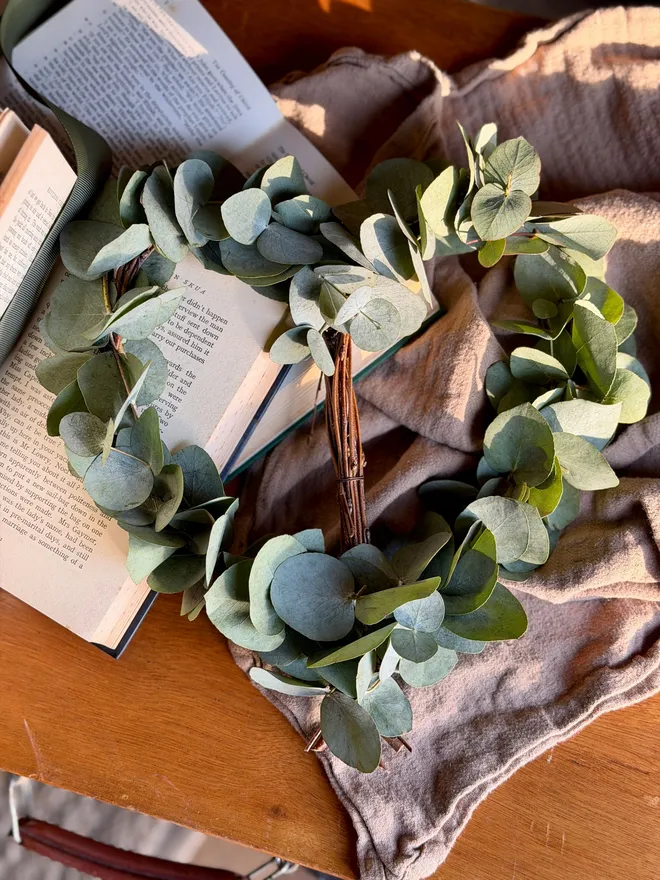 A frame of birch woven with sprigs of fresh eucalyptus. The leaves are a soft, muted green with a slightly silvery tone, round in shape. They cluster gently rather than covering the whole heart, so you can still see the wooden structure underneath.