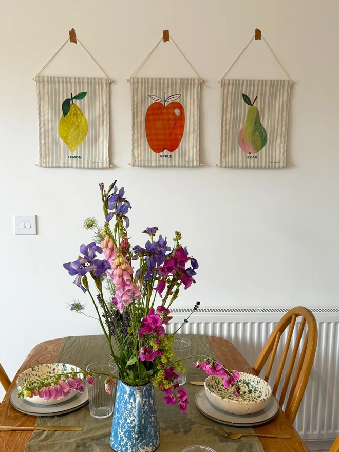 Cotton Lemon Wall Hanging, hanging on a white wall next to other fruit. 