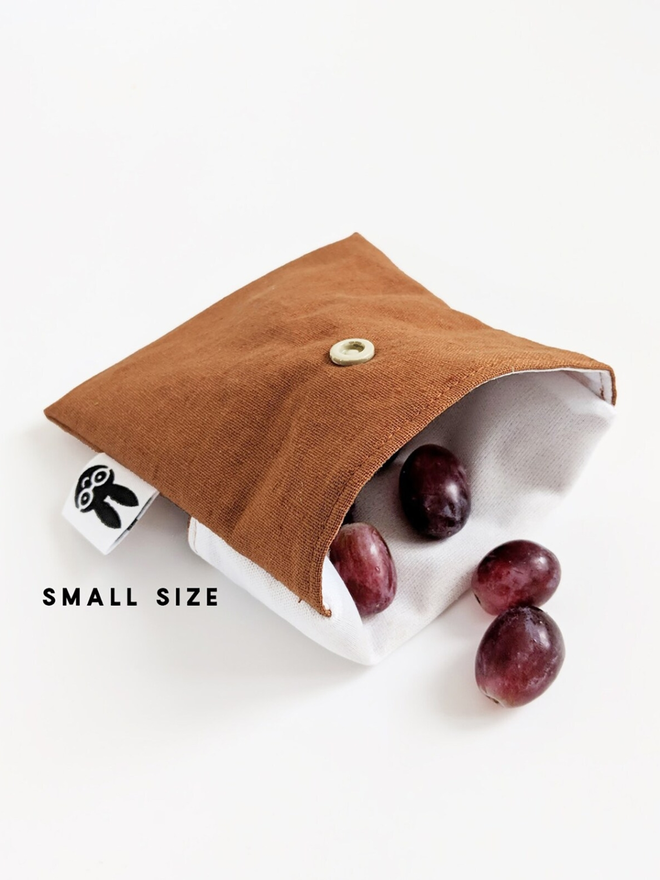 reusable linen snack pouch. a rust brown pouch holding grapes.