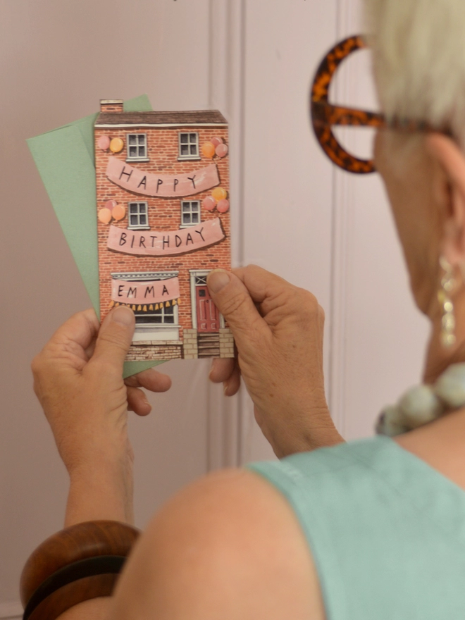 A house shaped birthday card being held by an artist women.