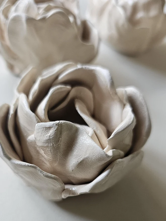 hand-sculpted ceramic flower in a soft cashmere glaze, featuring individually crafted petals and natural texture. Each unique piece is wall-mountable with a carved keyhole on the back