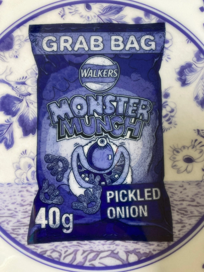 Close up of an 8" blue and white 'Delft' style plate featuring a packet of Monster Munch