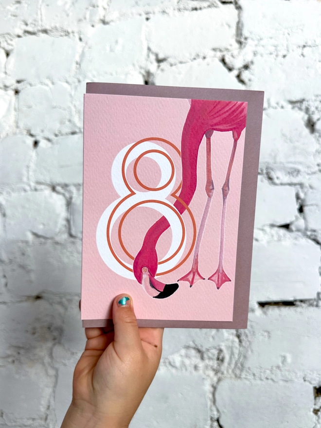 a pink card with a big white number 8 and an illustrated flamingo with a purple envelope