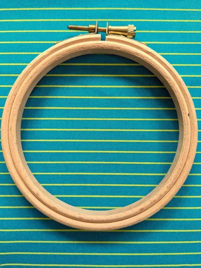 A wooden embroidery hoop lying on a stripy teal fabric