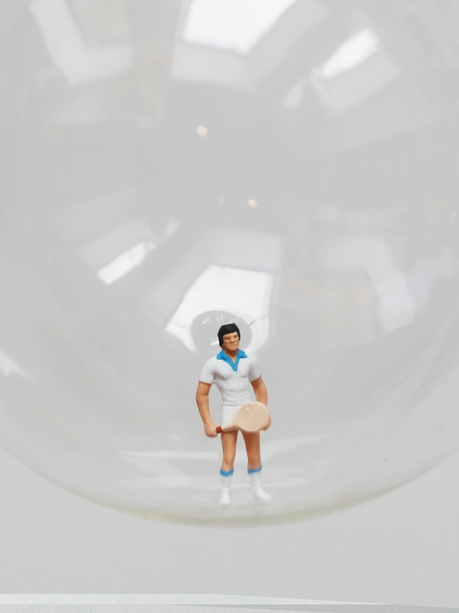 Miniature figure of a male tennis player in a glass Christmas bauble - close up 
