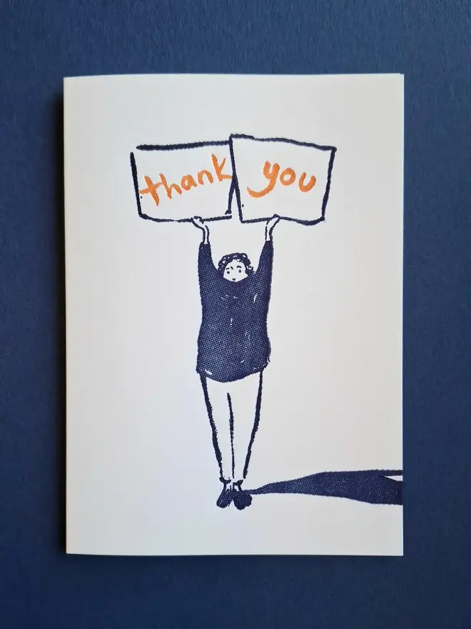 'Thank You' Letterpress Handprinted Greetings Card, a white thank you card with a blue design and orange writing sitting on a blue surface. 