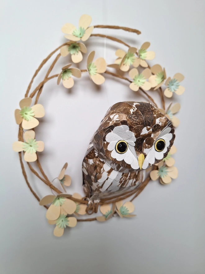 side view of a boreal owl handmade paper sculpture, on a wreath of soft yellow tree blossom flowers