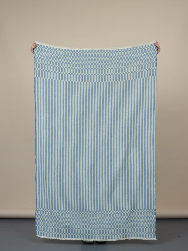 cham lambswool blanket. a blue and yellow striped blanket photographed against a plain wall.