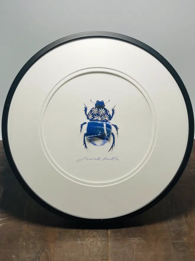 Hand-drawn, painted, mosaic clay, vintage Willow Tree pottery insect on white double mounted card, in a black circular frame.