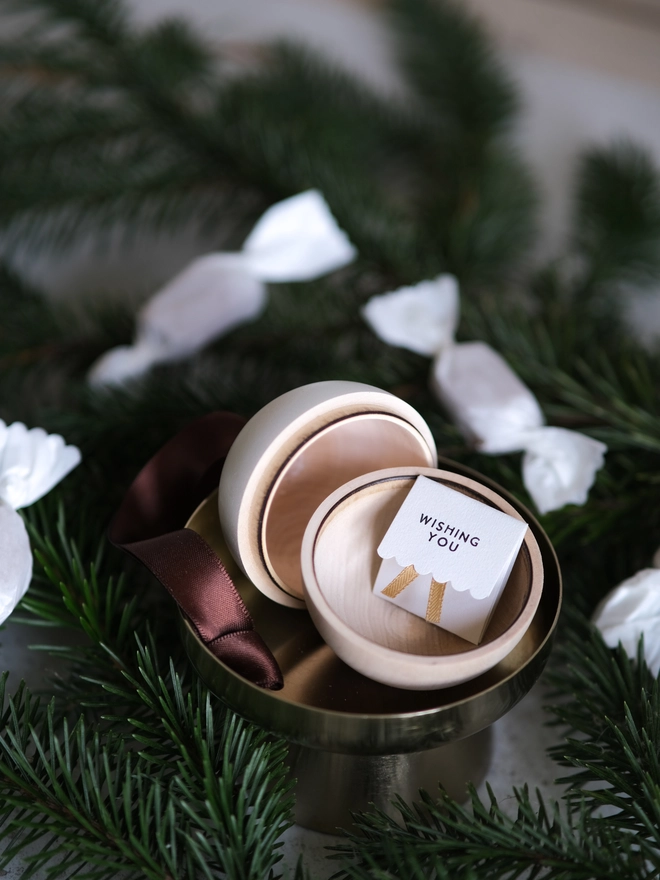 Wooden and white Christmas gift bauble with a removable lid, hanging from a Christmas tree with a space inside for a handwritten message, gift or surprise