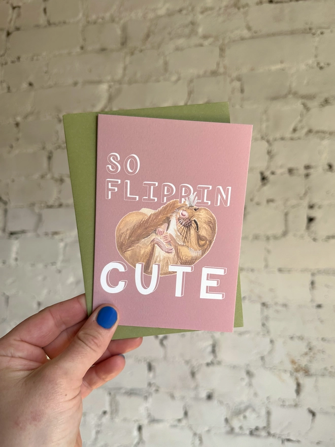 a dusty pink greetings card featuring an illustration of a sleeping mouse with the text “so flippin cute” with a green envelope