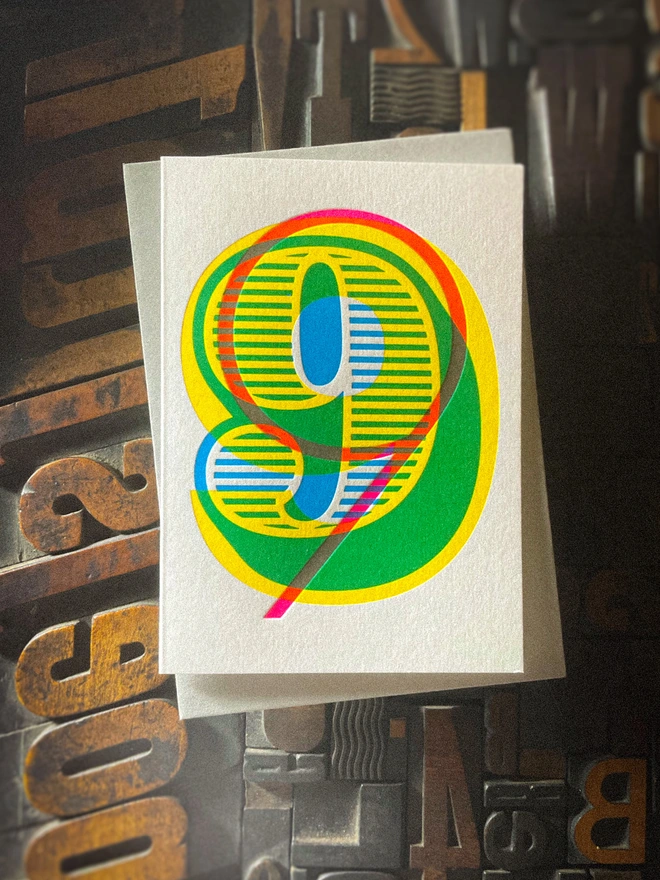 Handmade letterpress 9th birthday card featuring bold overlapping numerals printed in vibrant fluorescent cyan, magenta and yellow inks. Each card is individually hand printed using traditional letterpress techniques on luxury paper stock, creating a beautifully tactile finish with a deep impression and rich layered colours inspired by the CMYK printing process. Printed on a traditional letterpress from 1915. A wonderful artisan printed birthday card.