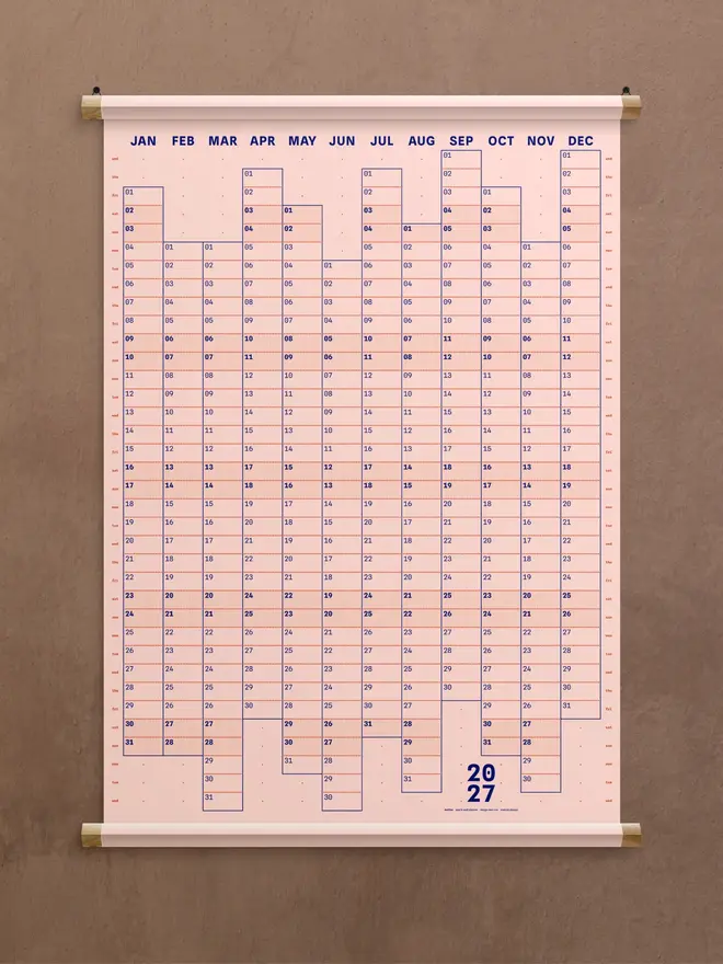 A pink 'nude' Dotline 2027 yearly wall planner on brown wall
