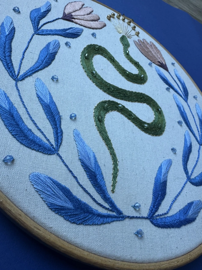 Close up of an embroidered snake surrounded by blue leaves and beads 