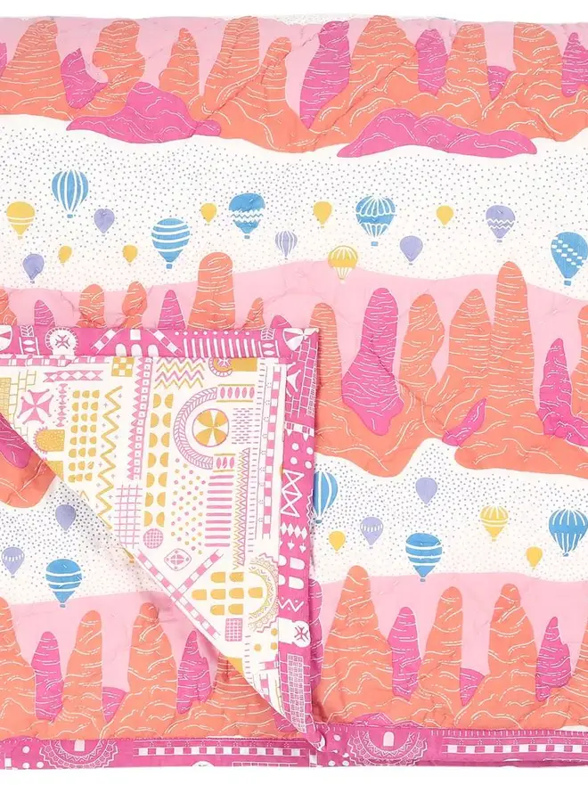 Fairy Chimney Quilt, a pink and yellow quilt sitting on a bed in a bedroom. 