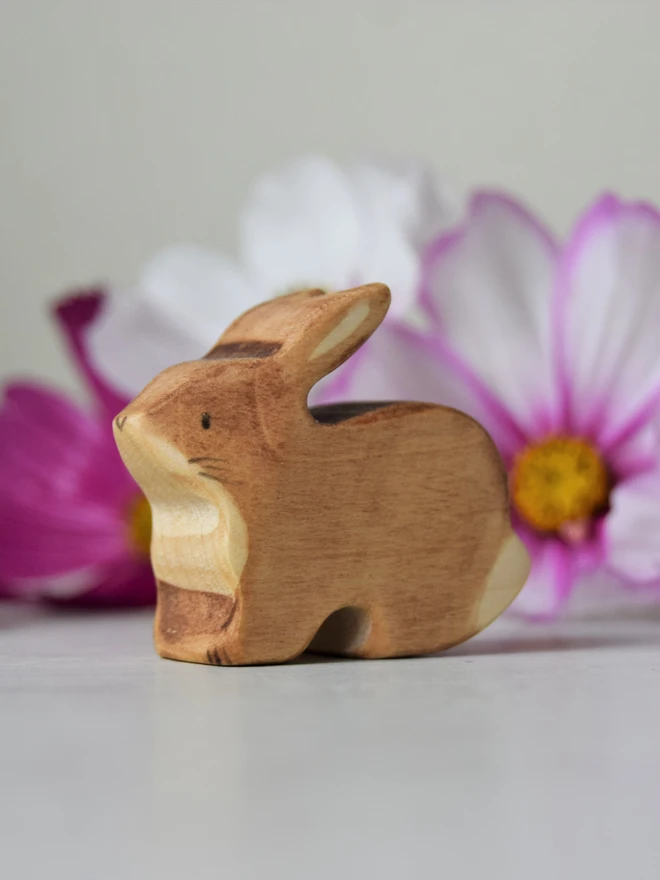 wooden brown rabbit toy made by eric and albert sitting by some flowers