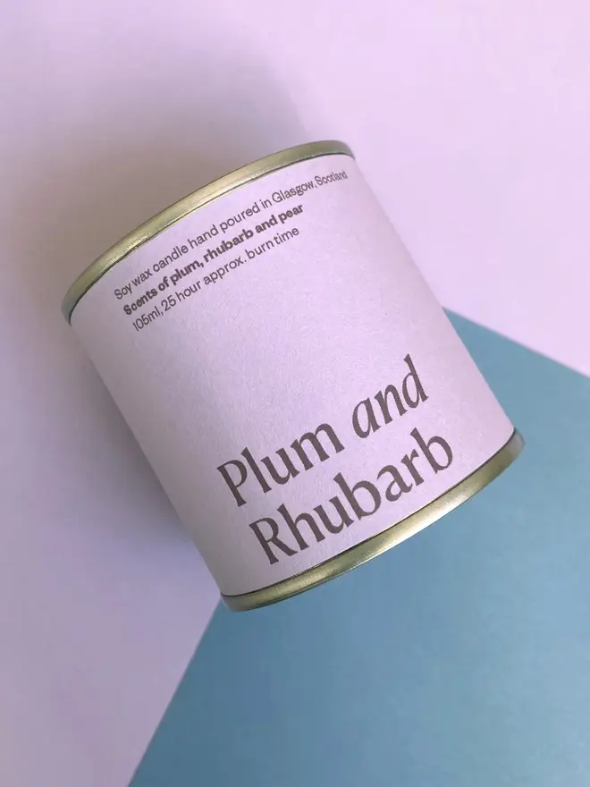 lum & Rhubarb Soy Wax Candle Tin, against a purple and blue background. 
