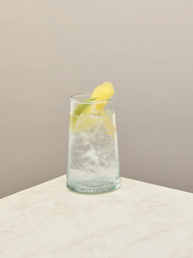 Highball Glasses (Set Of 1 Or 4), a highball glass sitting on a plain counter top against a white backdrop. It is filled with a soft drink. 