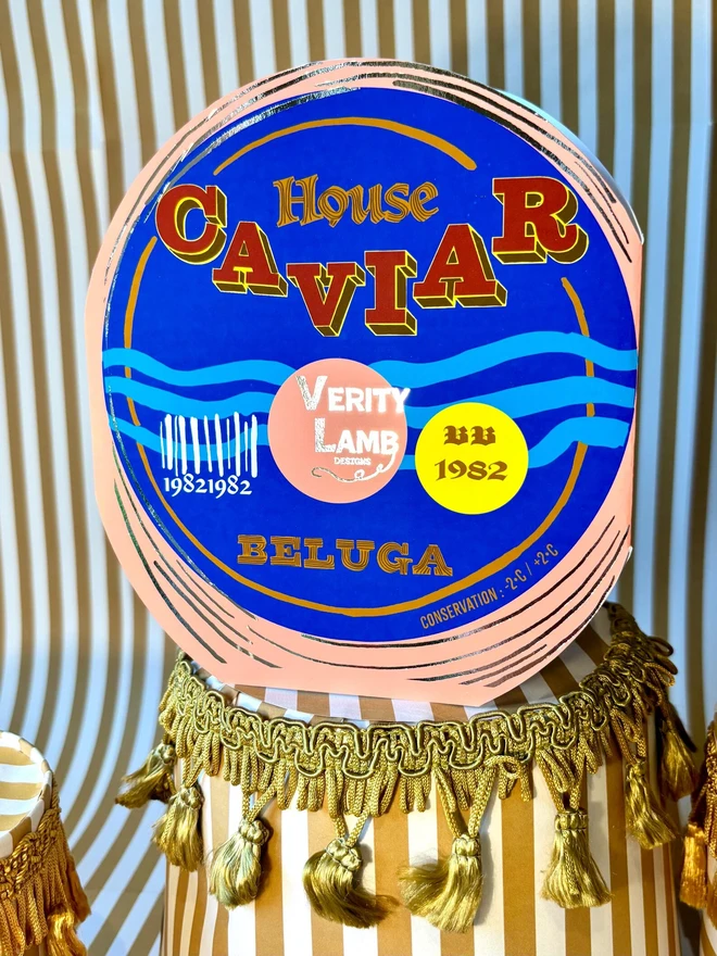 Caviar Tin Card, a colourful card sitting on a decorated display in front of a backdrop. 