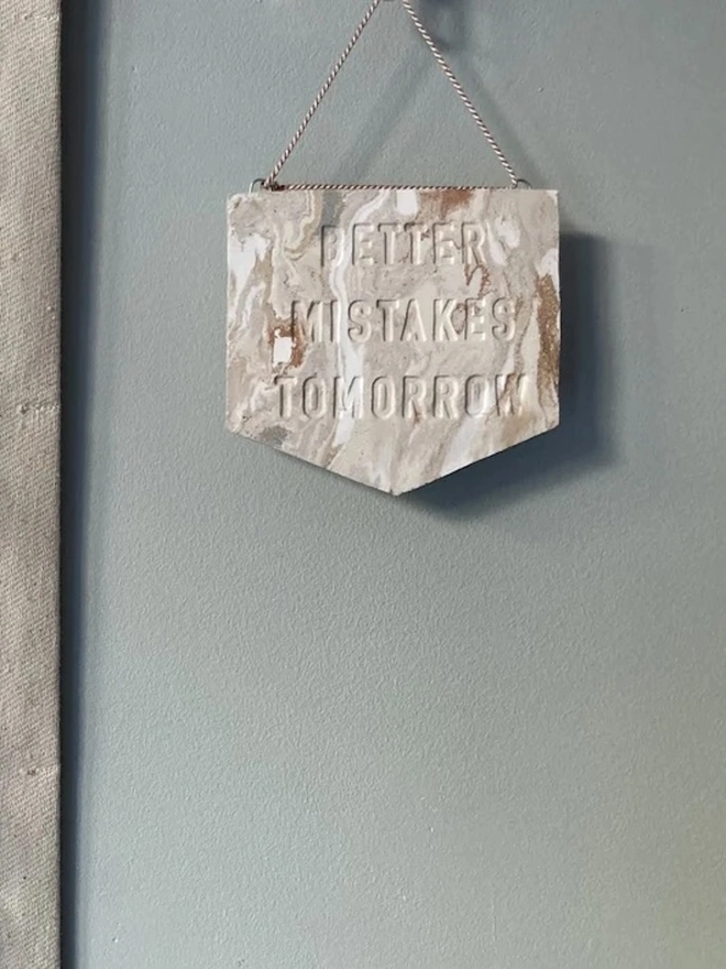 'Better Mistakes Tomorrow' Banner, a clay banner hanging against a plain backdrop.