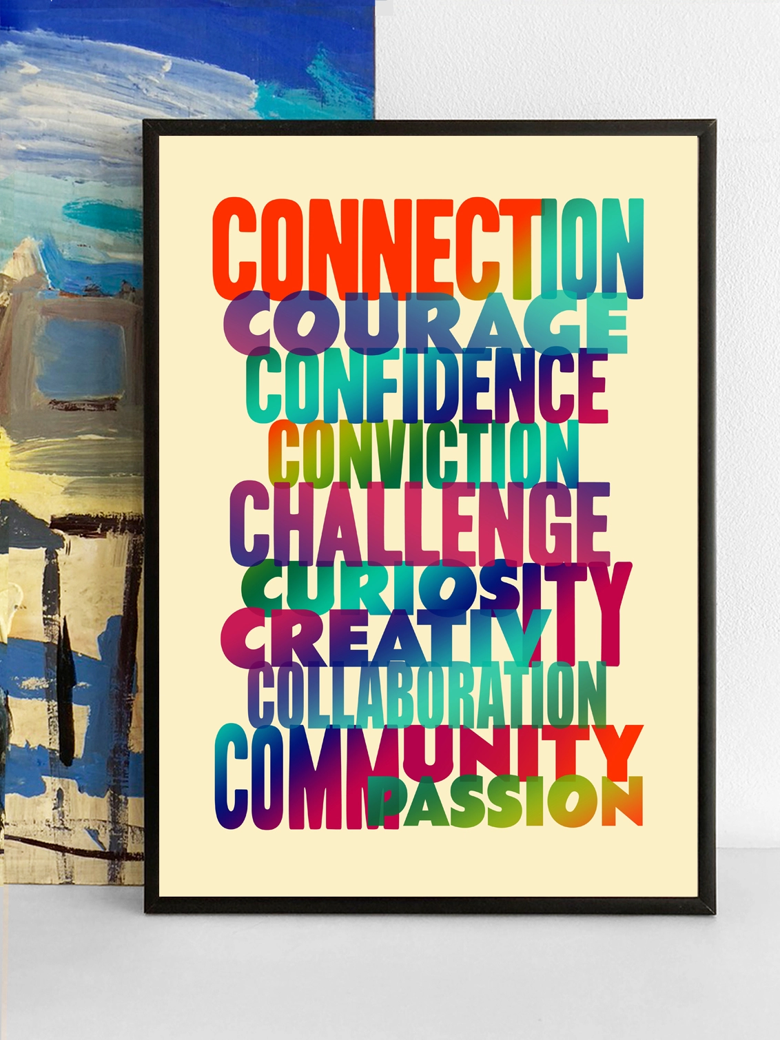 Framed multicoloured typographic print of “Connection Courage Confidence Conviction Challenge Curiosity Creativity Collaboration Community Compassion” Words by Shiobahn Sheridan  The print rests against a blue and yellow abstract painting.
