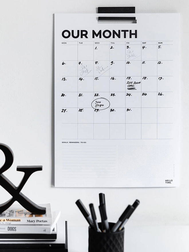 Year Wall Calendar on the wall with handwriting on it by a pile of books and pen pot