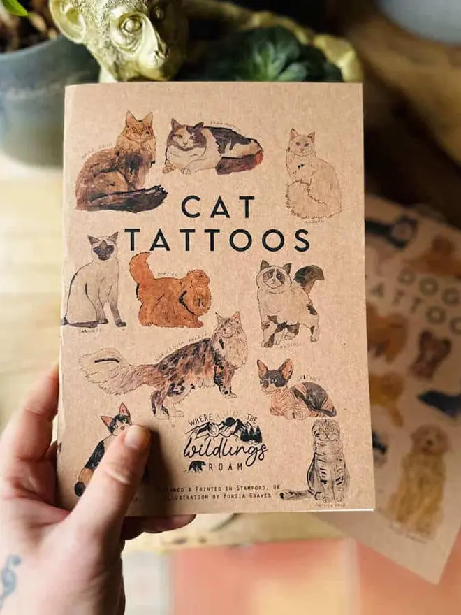 Pets Temporary Tattoos, a hand holds a brown kraft paper tattoo booklet titled "CAT TATTOOS."
