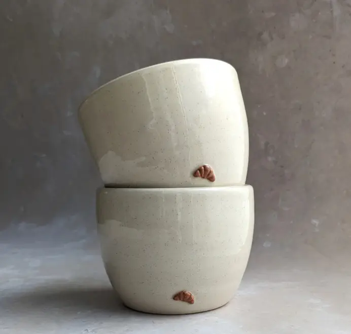 Two croissant coffee cups in vanilla bean glaze stacked together on a grey marble background.