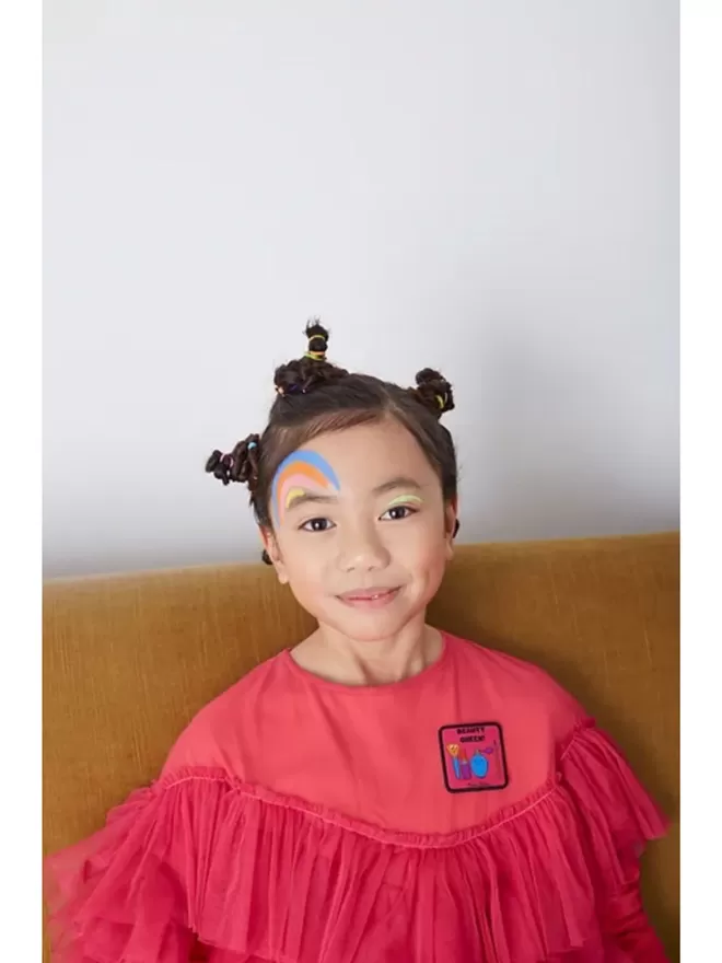 A kid with rainbow face paint wears the Beauty Queen Patch.