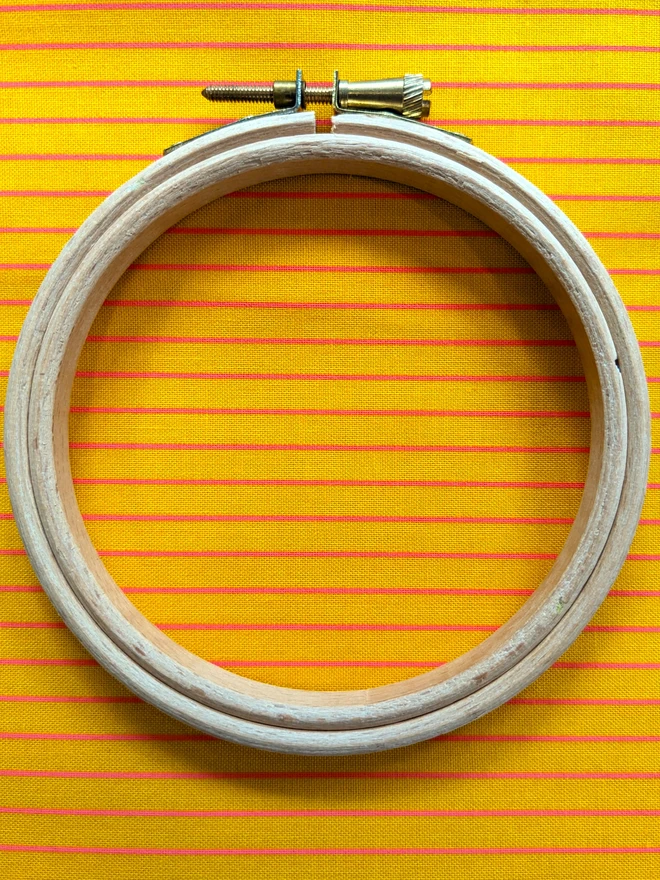 A wooden embroidery hoop lying on a stripy yellow/orange fabric