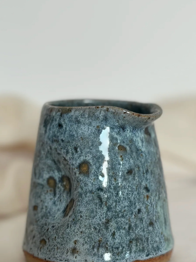 Pinch Jug. A Blue Mini Pinch Mug, close up, against a cream background.