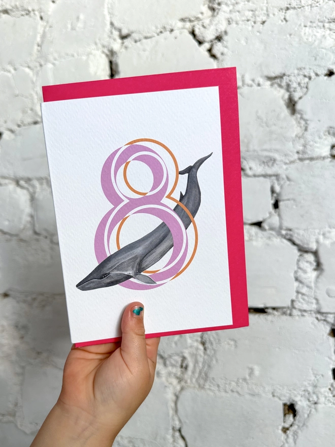 white card with a big pink number 8 and an illustration of a fin whale with a neon pink envelope