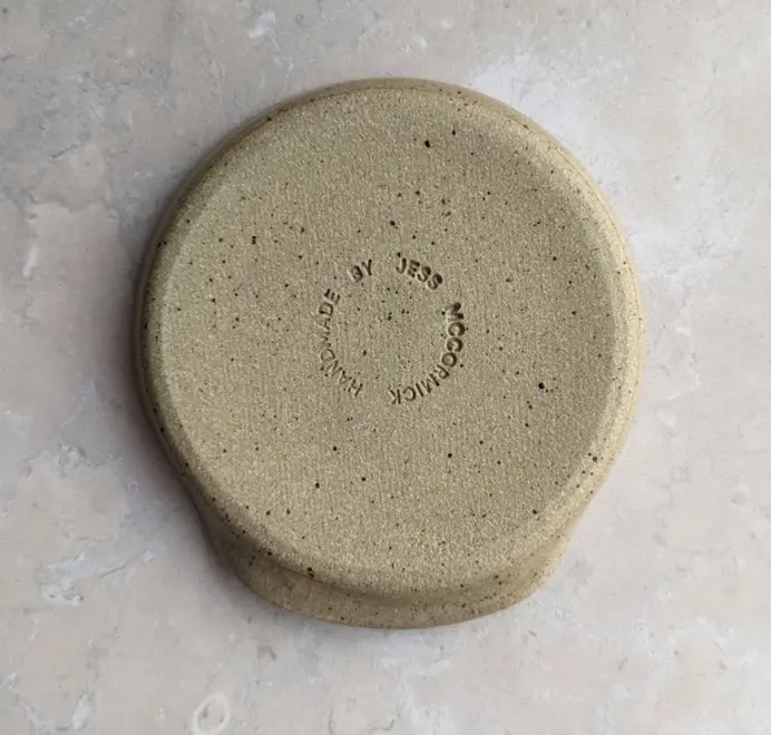 Croissant stoneware spoon rest in biscuit glaze against a grey marble background.