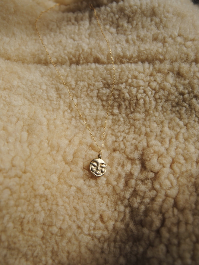 Image of gold toned hand carved moon face pendant, on gold chain, laying over sheepskin fleece 