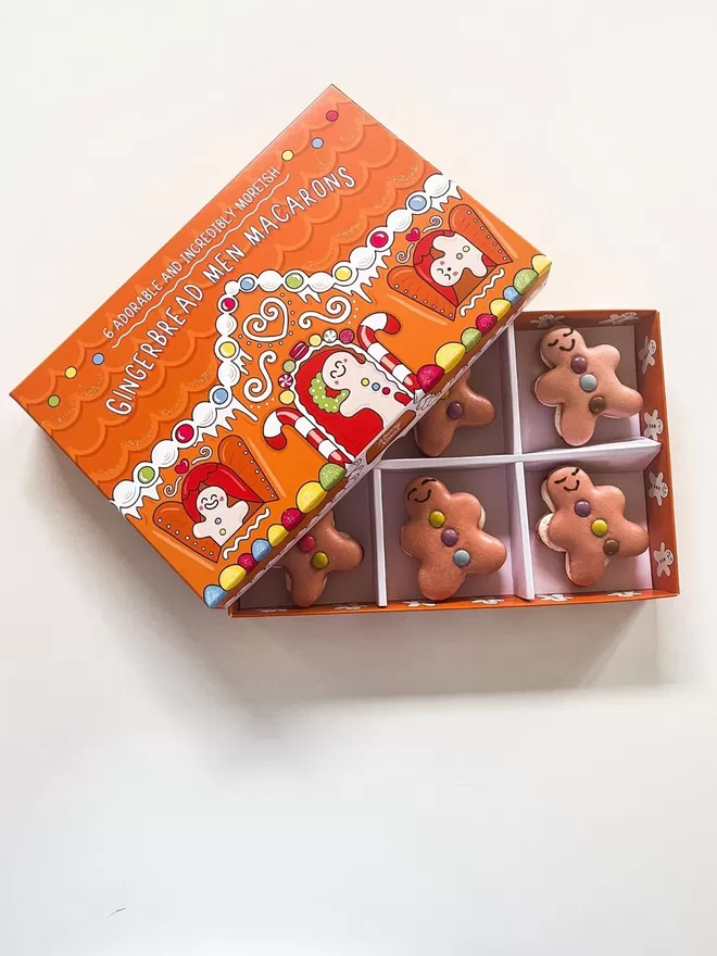 six gingerbread men macarons with smiley faces and colourful chocolate buttons sitting in a gingerbread house illustrated box