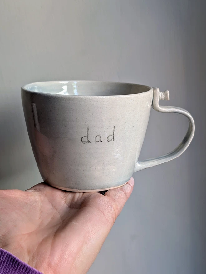 grey cup with screw on the mug handle and the word dad hand painted on the front