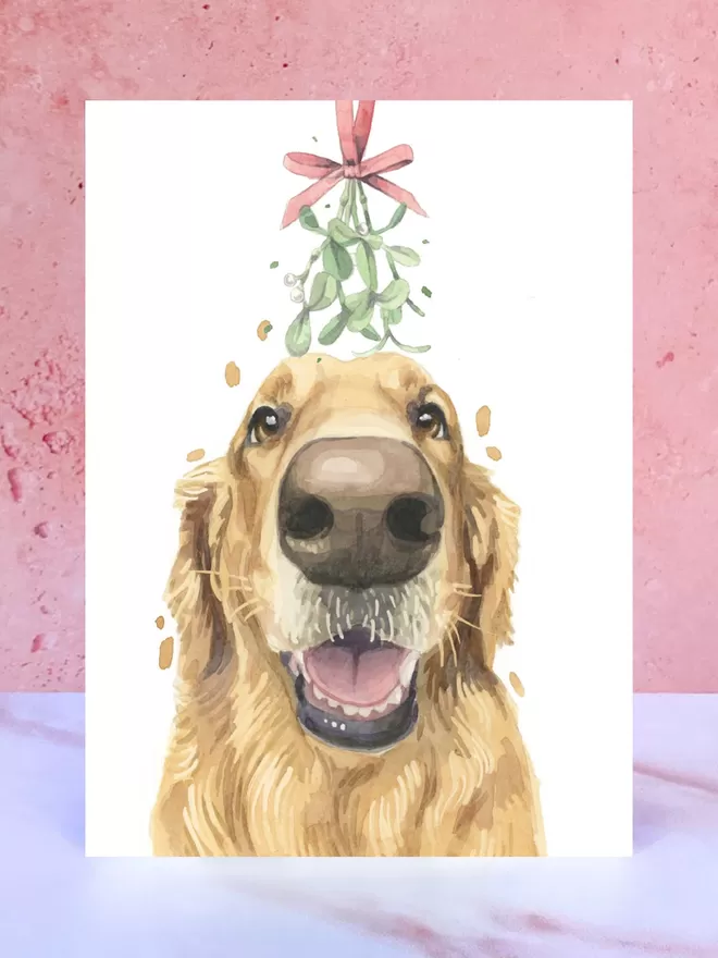 A Christmas card featuring a hand painted design of a Golden Retriever, stood upright on a marble surface.