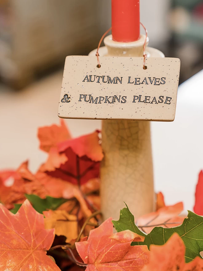 ceramic sign with autumn quote hung around an orange candlestick