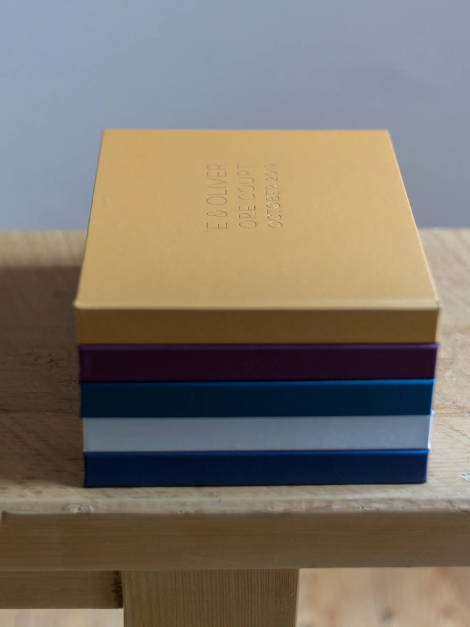 lots of guest books are stack up in a pile on the edge of a wooden table. On the top book you can see the personalisation