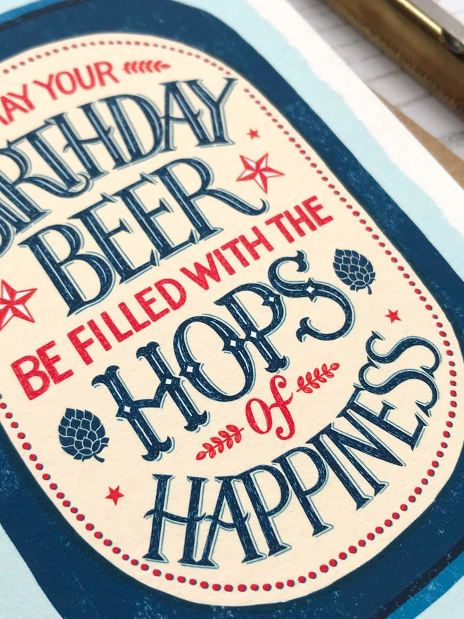 Illustrated beer can with hand lettered beer hops quote on a blue background close up detail