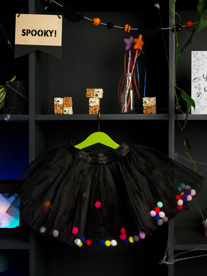 Black pom pom tutu with multicoloured pom poms hanging on a shelf, halloween tutu