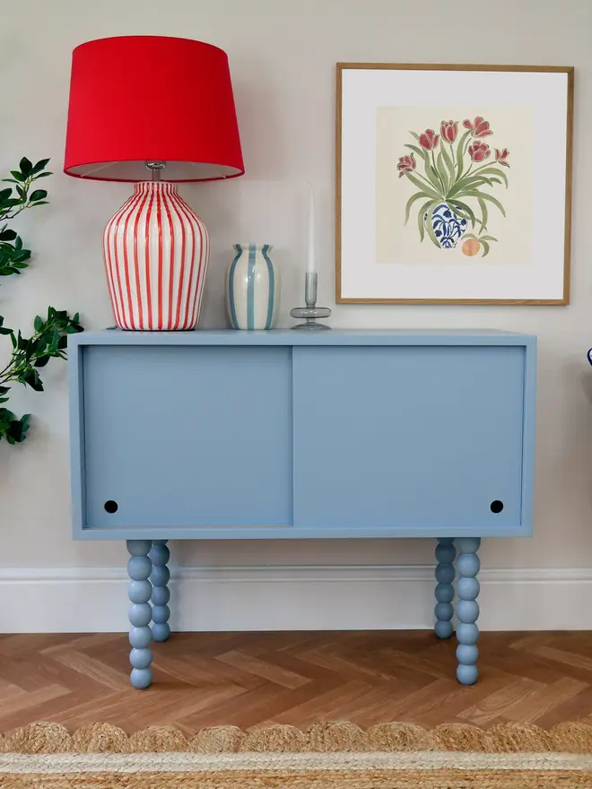Light blue cabinet with sliding doors and decorative bobbin-style legs in a cozy room.
