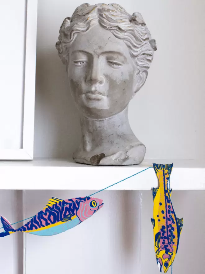 Multicoloured fish with bust of woman's head on white mantelpiece