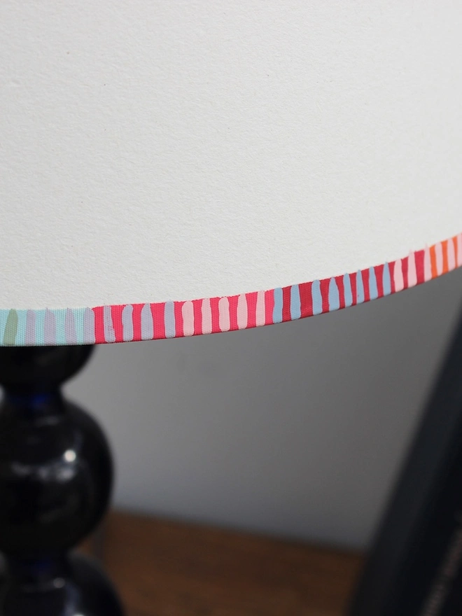A bold stripe lampshade with a playful, colourful striped border in pink, red, blue, and green. This pretty lampshade adds a pop of striped lighting detail, perfect for modern interiors and striped lampshades UK collections.