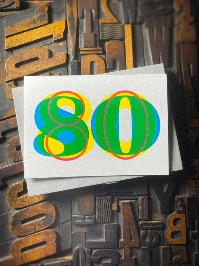 Handmade letterpress 80th birthday card featuring bold overlapping numerals printed in vibrant fluorescent cyan, magenta and yellow inks. Each card is individually hand printed using traditional letterpress techniques on luxury paper stock, creating a beautifully tactile finish with a subtle deboss and rich layered colours inspired by the CMYK printing process.