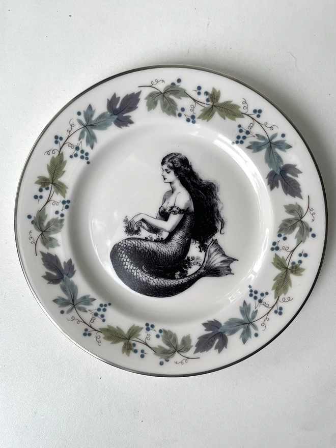 vintage plate with an ornate border, with a printed vintage illustration of mermaid in the middle