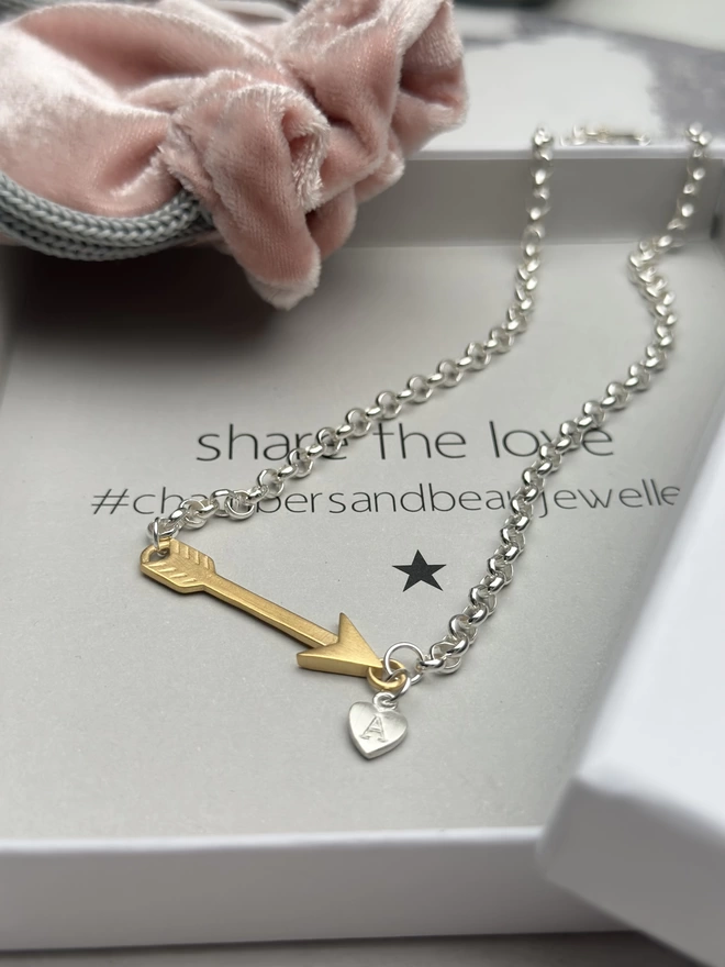 A gold arrow charm hangs horizontally from a sterling silver chain with a personalised silver mini heart charm