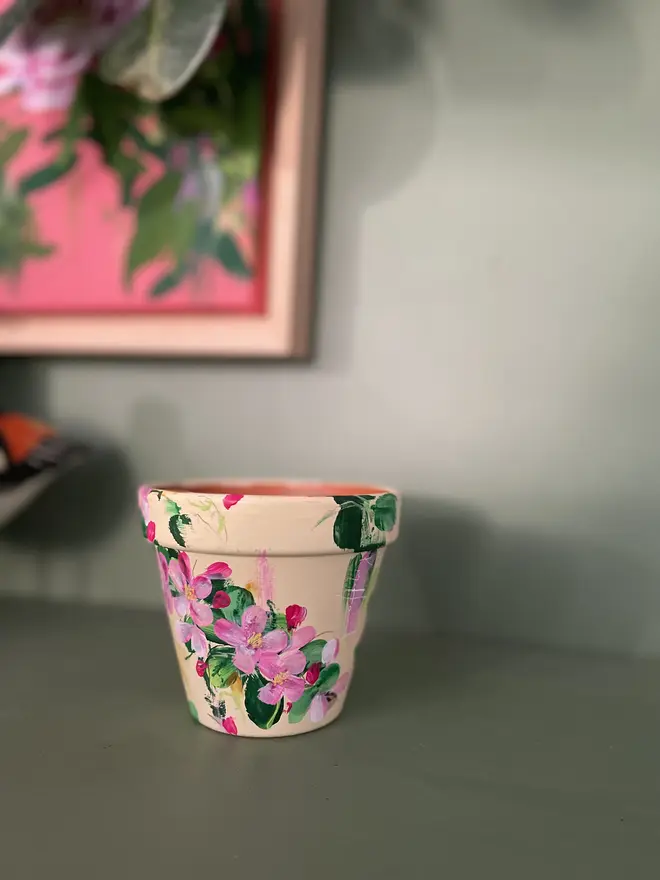 hand painted terrecotta floral plant pot background in a pale yellow with pink and white blossom flowers