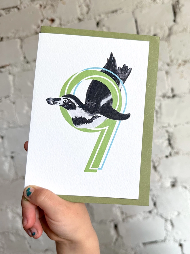 white card with a big green number 9 and a penguin illustration and a green envelope