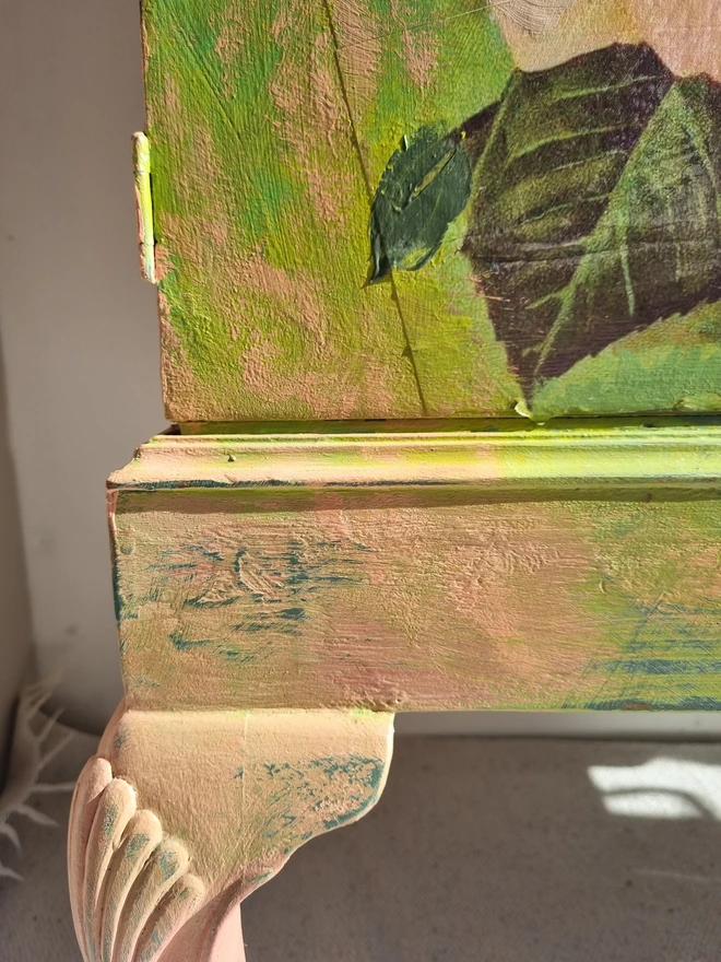 A painted record cabinet decorated with a sci fi image from the 1950s of a lady running from an alien and on the other door, a rose taken from a Victorian seed packet. There is wording that runs down the middle of the cabinet which reads 'it could be worse'. The colours are apple green and pinks.